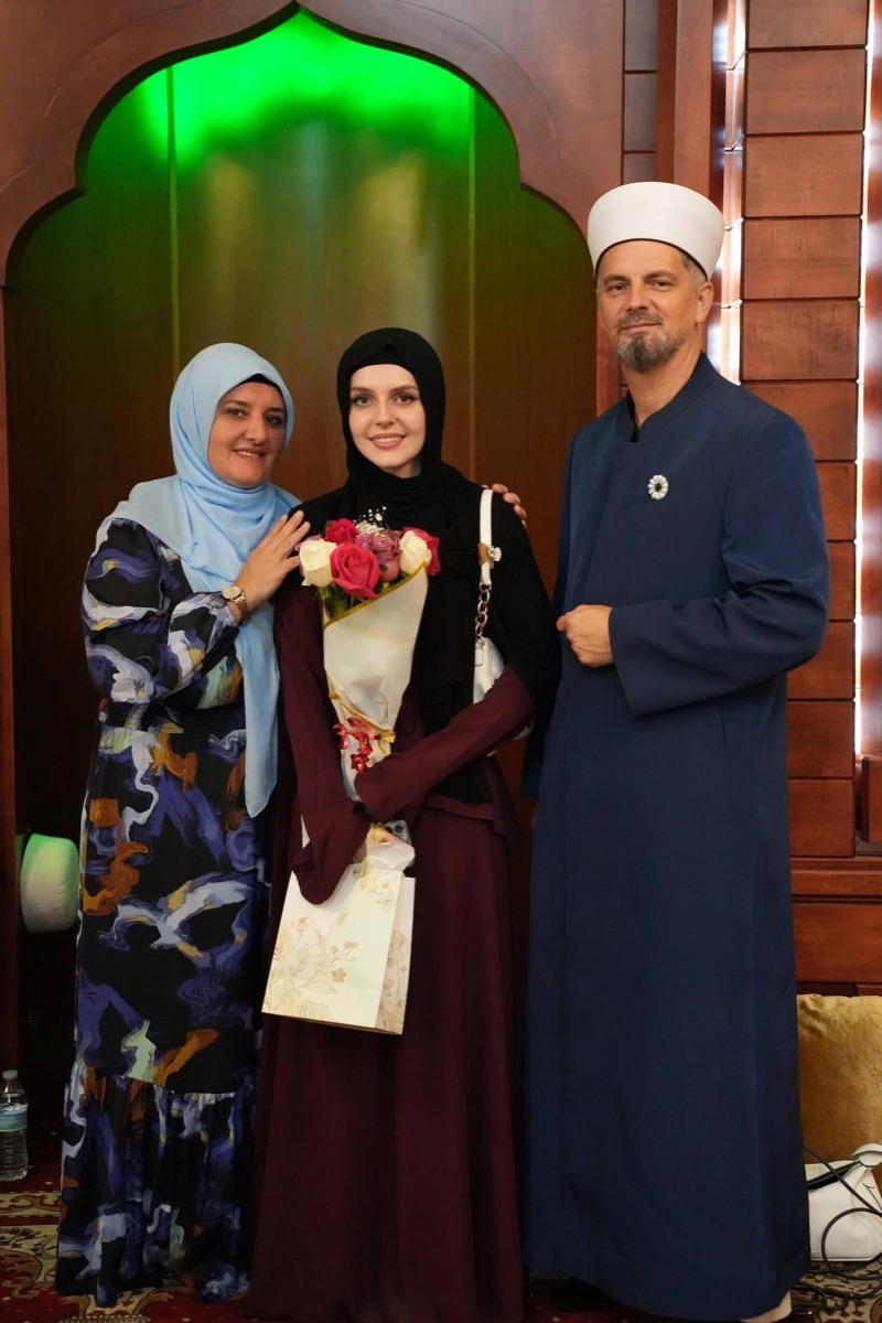 The imam with a young woman holding flowers and her mother at the end-of-year mekteb celebration